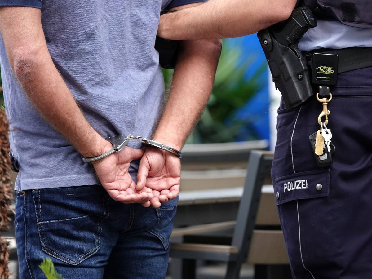 Ein Mann steht in Handschellen neben einem Polizisten.
