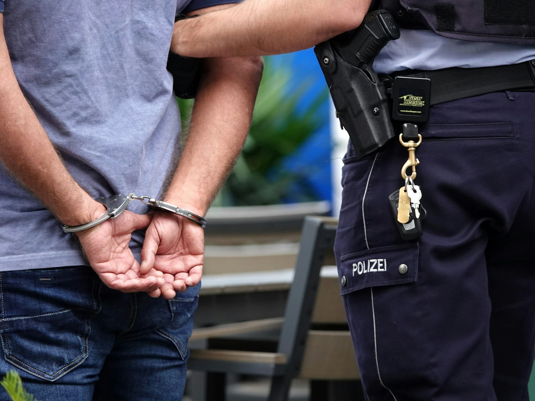 Ein Mann steht in Handschellen neben einem Polizisten.