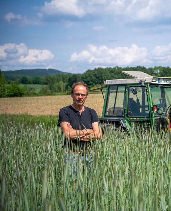 Ulf Allhoff-Cramer, Landwirt, steht in einem Roggen-Feld vor seinem Traktor.