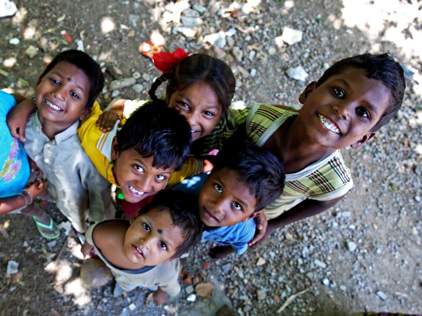Unser Symbolfoto vom 24. Mai 2016 zeigt sieben indische Kinder, die in die Kamera blicken. Manche lächeln, andere schauen ängstlich. Sie stehen auf einem sandigen Untergrund mit Scherben, Steinen und Müll.