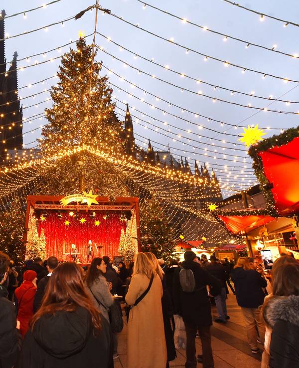 Auf dem Weihnachtsmarkt am Kölner Dom flanieren Besucherinnen und Besucher unter einem „Himmel“ aus Lichterketten.