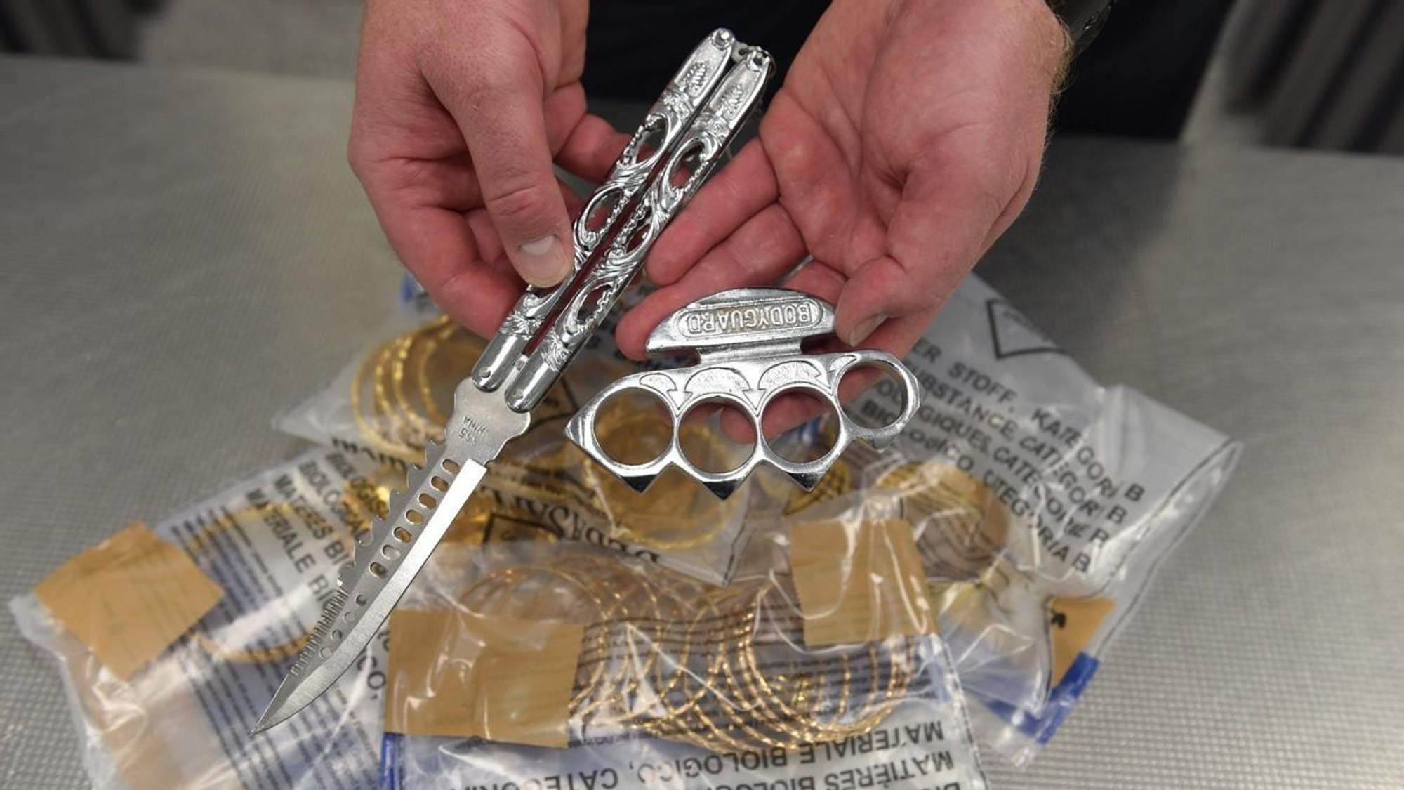 Eine Person hält einen Schlagring und ein Springmesser in die Kamera.