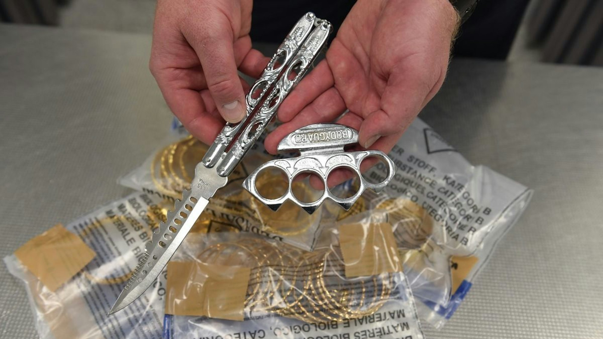 Eine Person hält einen Schlagring und ein Springmesser in die Kamera.