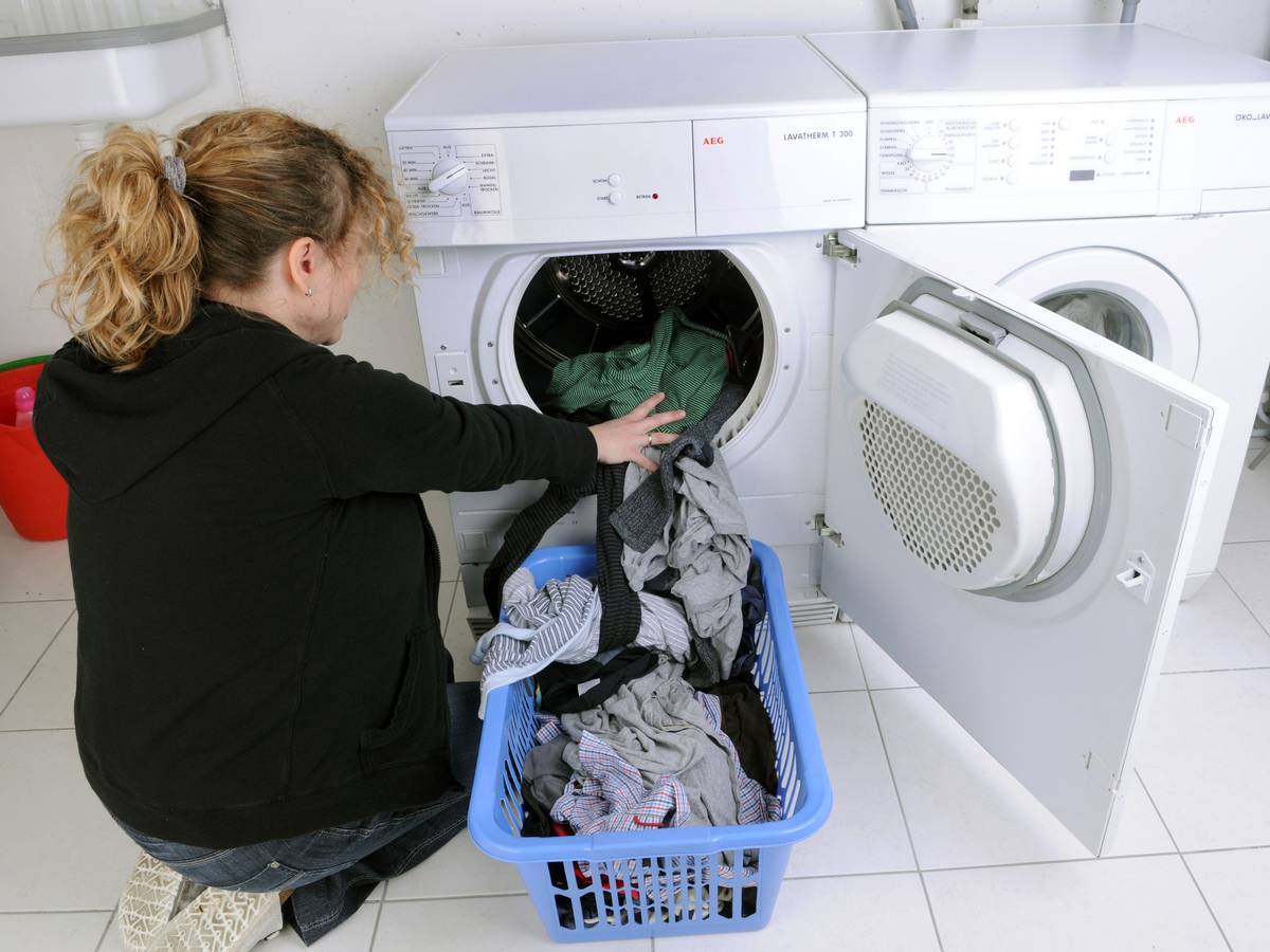 Eine Hausfrau befüllt einen Wäschetrockner mit frisch gewaschener Kleidung.