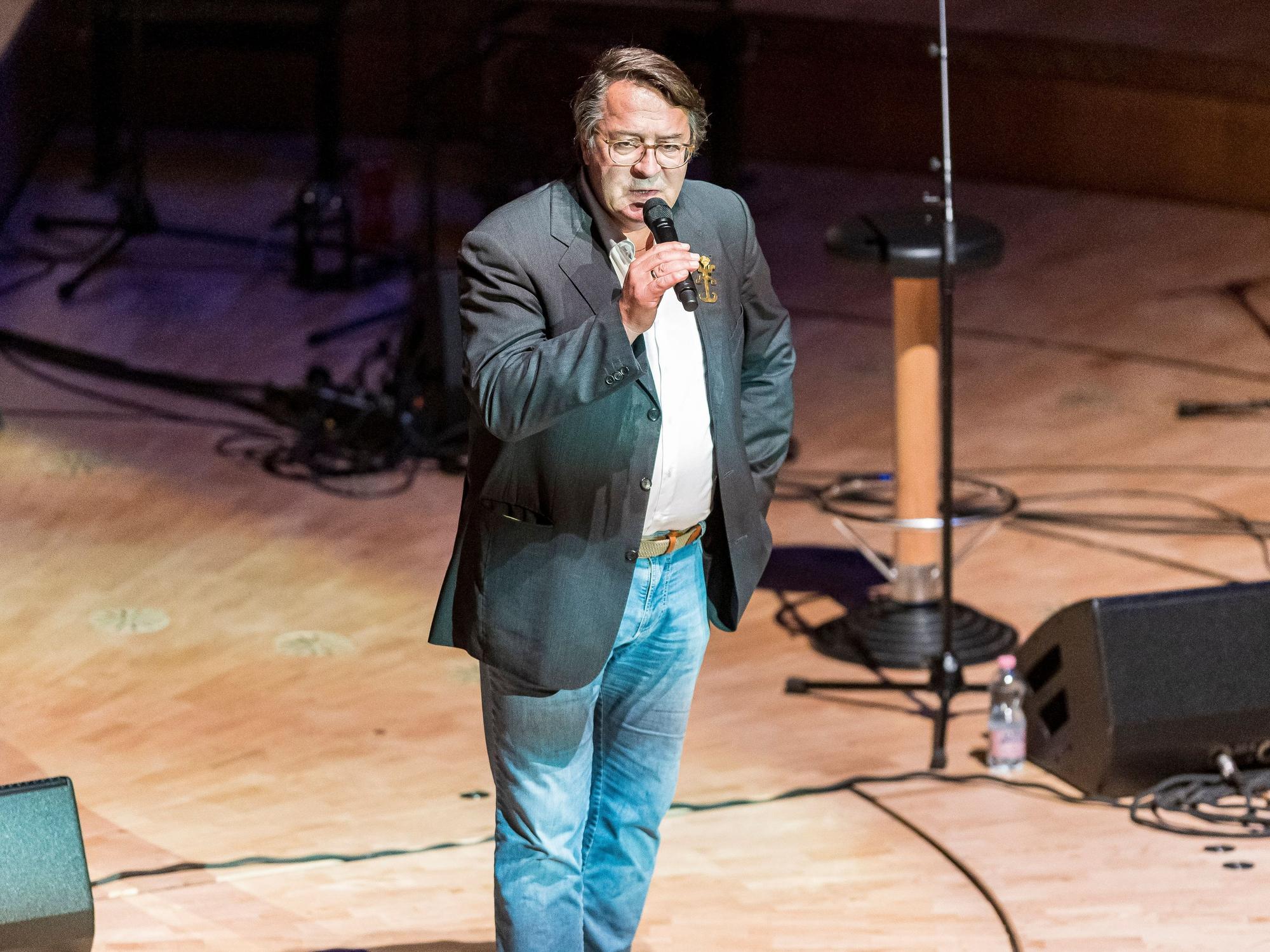 Hans Mörtter steht mit einem Mikrofon auf der Bühne der Kölner Philharmonie.