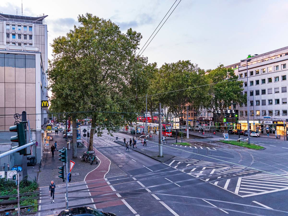 Menschen und Autos auf dem Barbarossaplatz in Köln in der Dämmerung.