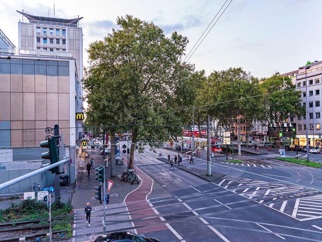 Menschen und Autos auf dem Barbarossaplatz in Köln in der Dämmerung.