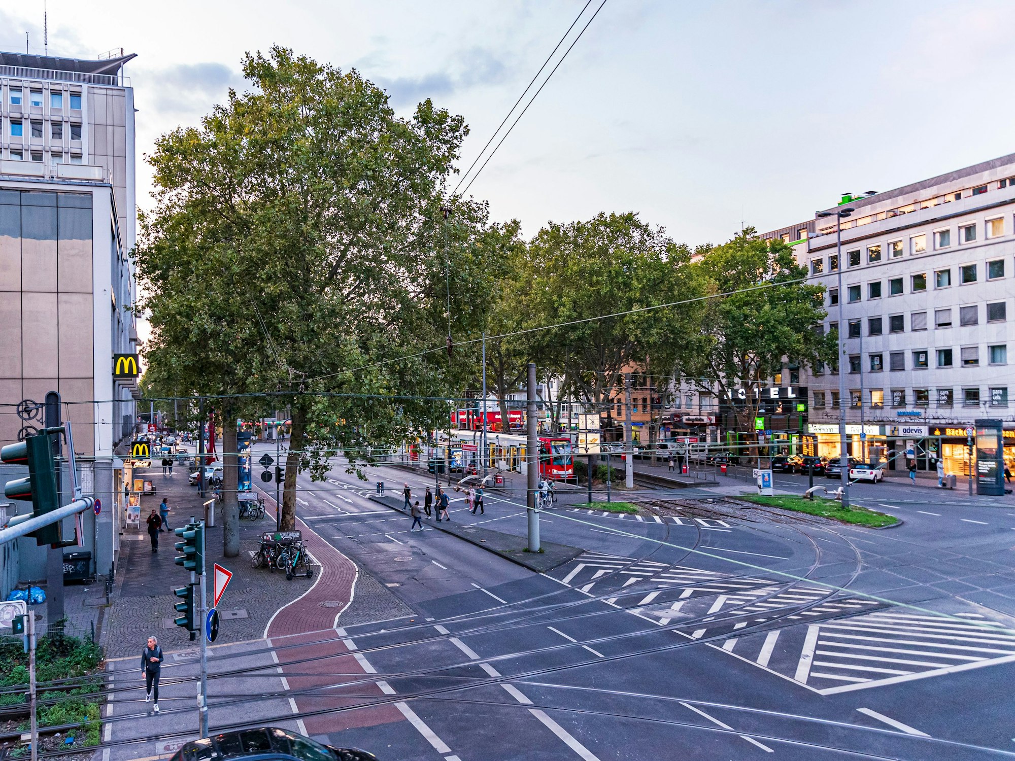 Menschen und Autos auf dem Barbarossaplatz in Köln in der Dämmerung.