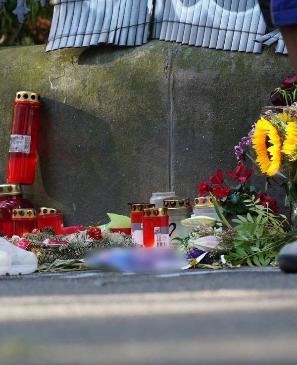 Zwei Menschen stehen an einem Zaun, an dem mit Kerzen und Blumen eines von der Polizei erschossenen Jugendlichen gedacht wird.