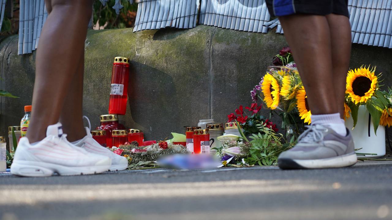 Zwei Menschen stehen an einem Zaun, an dem mit Kerzen und Blumen eines von der Polizei erschossenen Jugendlichen gedacht wird.