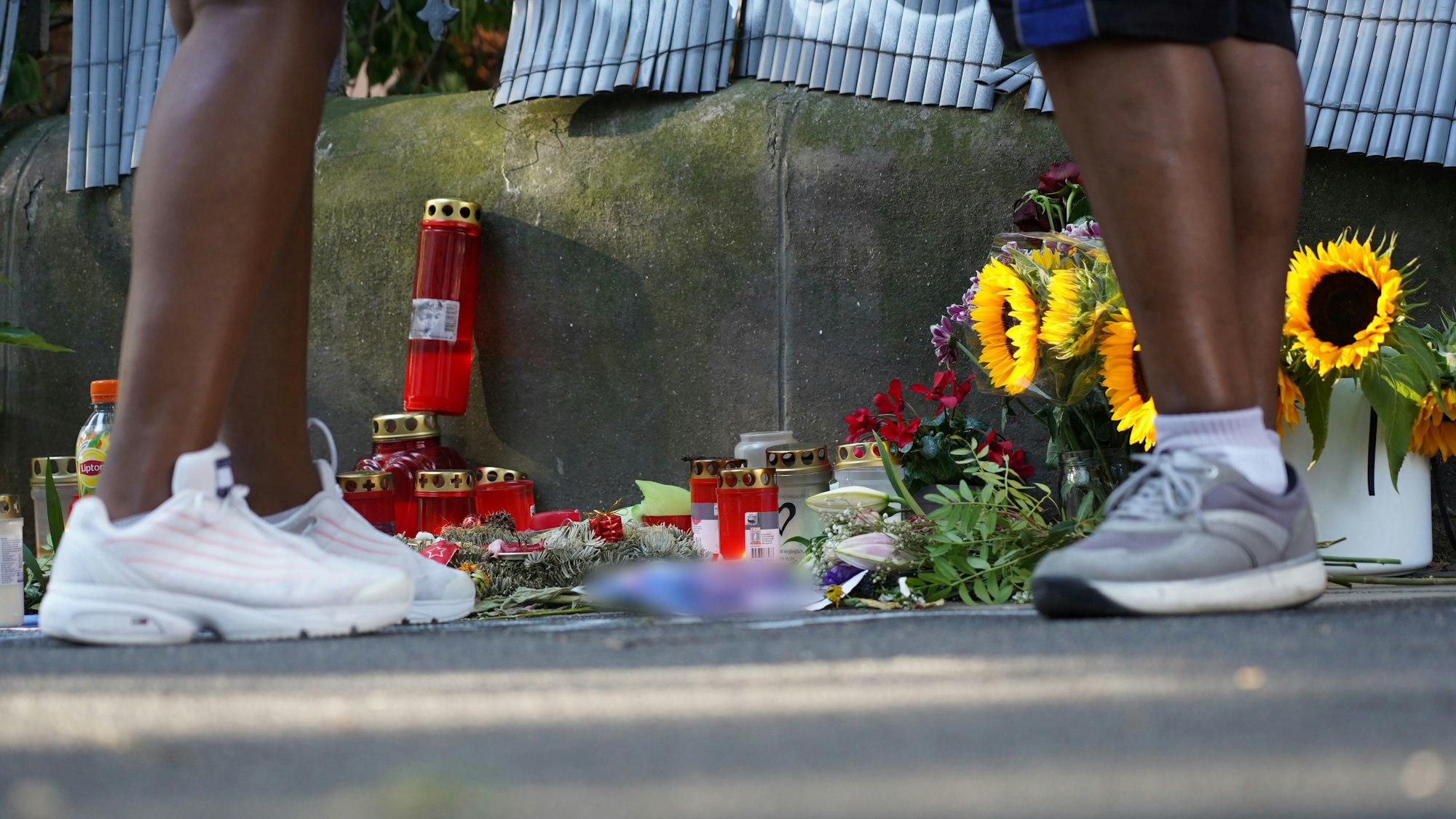 Zwei Menschen stehen an einem Zaun, an dem mit Kerzen und Blumen eines von der Polizei erschossenen Jugendlichen gedacht wird.