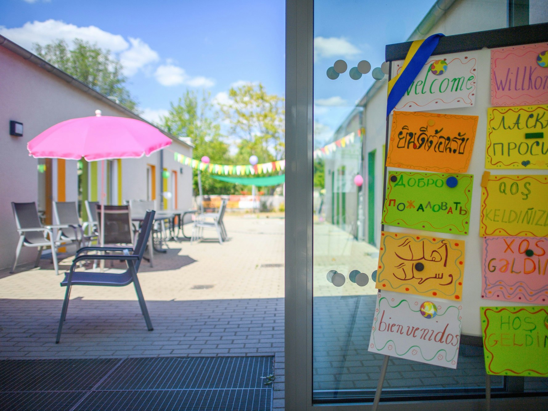 Zettel an einer Wand in einer Kita, von Kindern geschrieben. Dahinter ein Spielplatz.