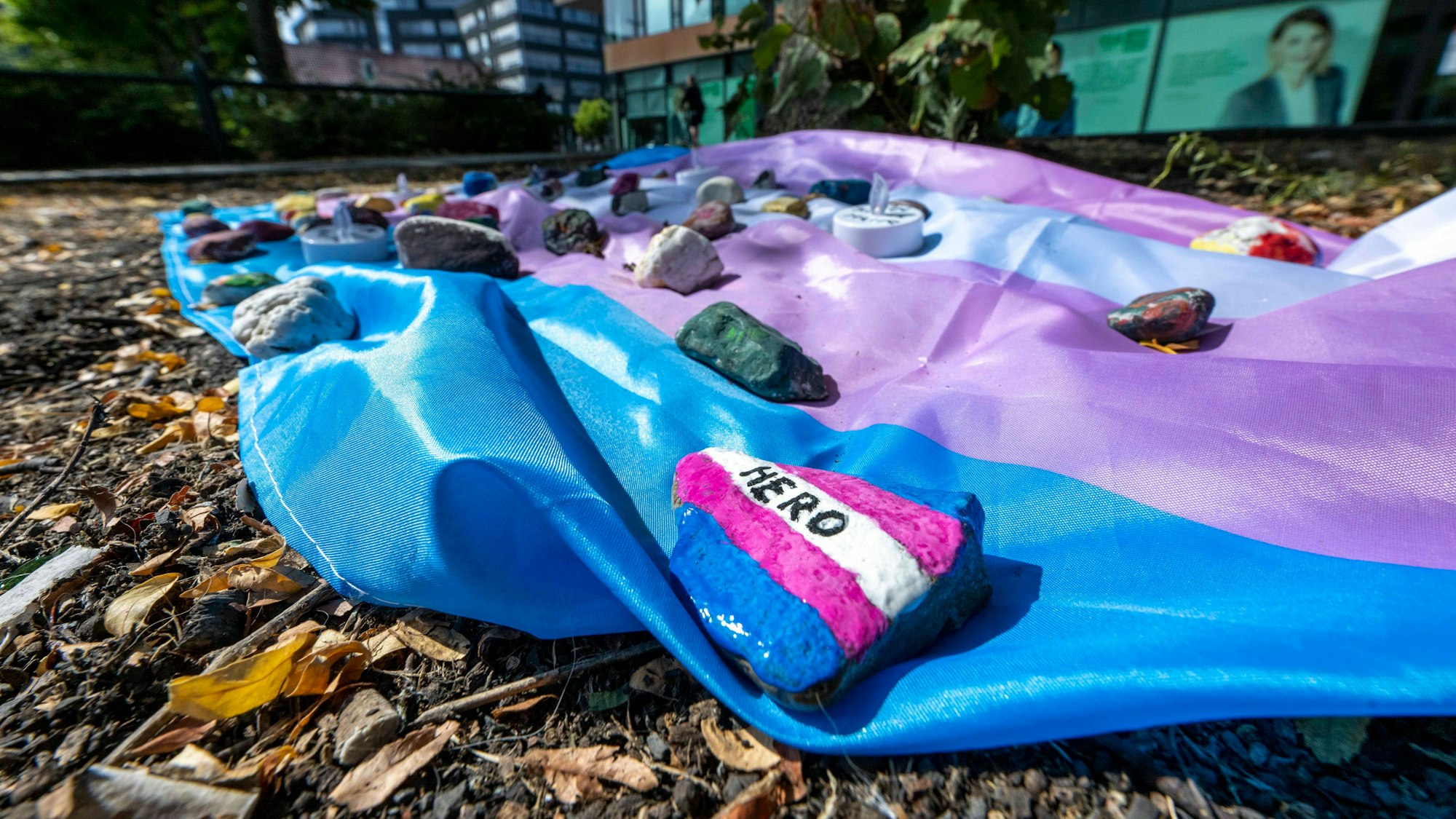 Menschen haben auf dem Hafenplatz eine Fahne ausgelegt, die mit bemalten Steinen beschwert ist. Ein 25 Jahre alter Mann, der in Münster am Rande einer Versammlung des Christopher-Street-Days von Unbekannten niedergeschlagen wurde, ist gestorben.