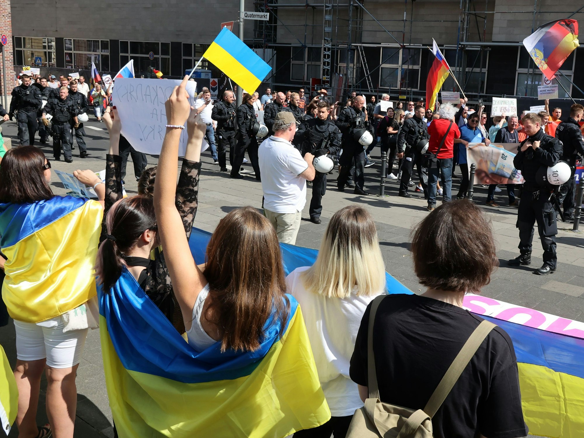 Demonstrantinnen hissen bei einer Kundgebung die ukrainische Flagge.