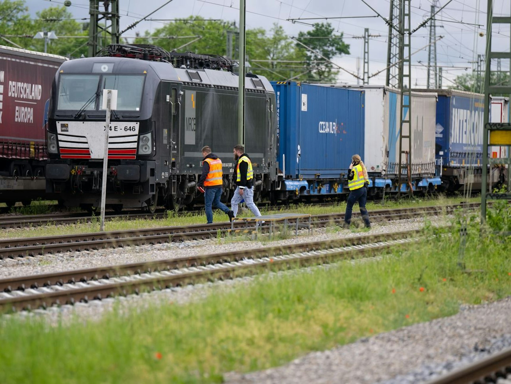 Menschen gehen durch einen Güterbahnhof und suchen nach Spuren.