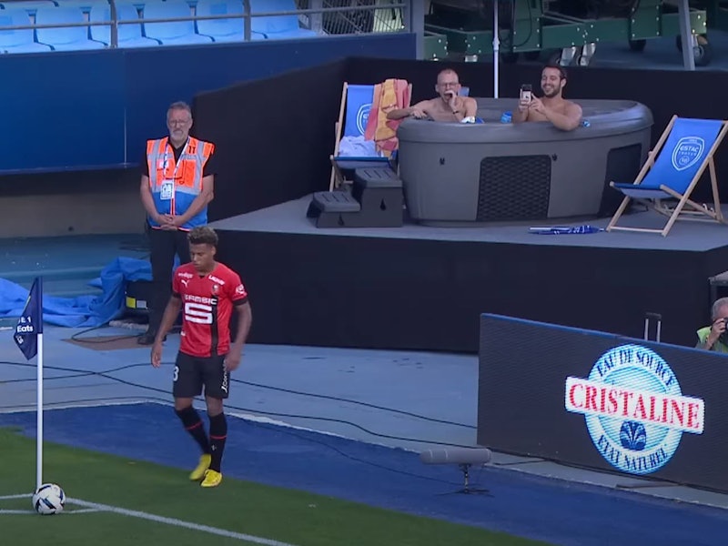 Zwei Fans von ESTAC Troyes sitzen beim Spiel gegen Stade Rennes in einem Jacuzzi am Spielfeldrand in einer Ecke des Stadions.