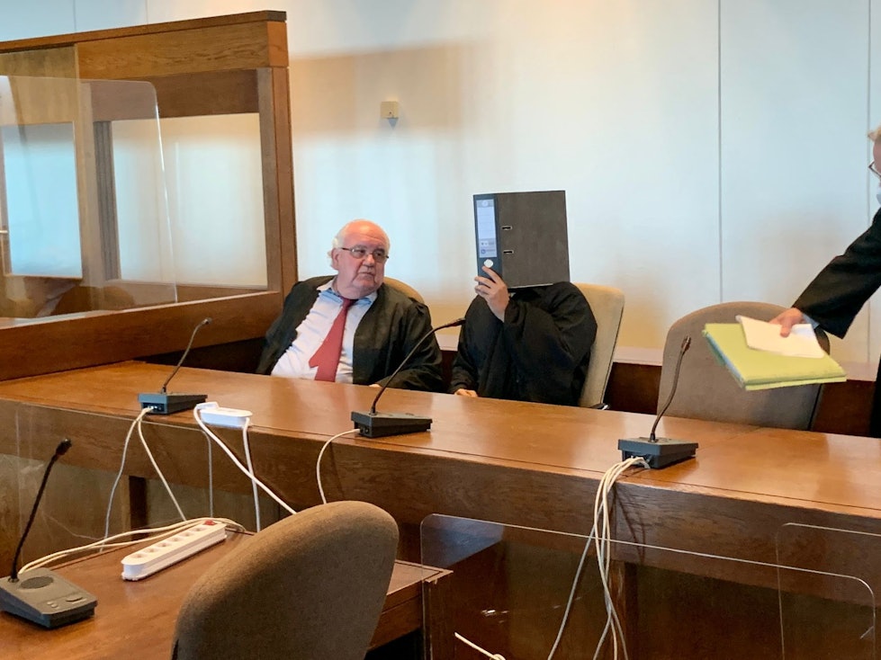 Der angeklagte Anil G. versteckt sich zwischen seinen Anwälten hinter einem Aktenordner.