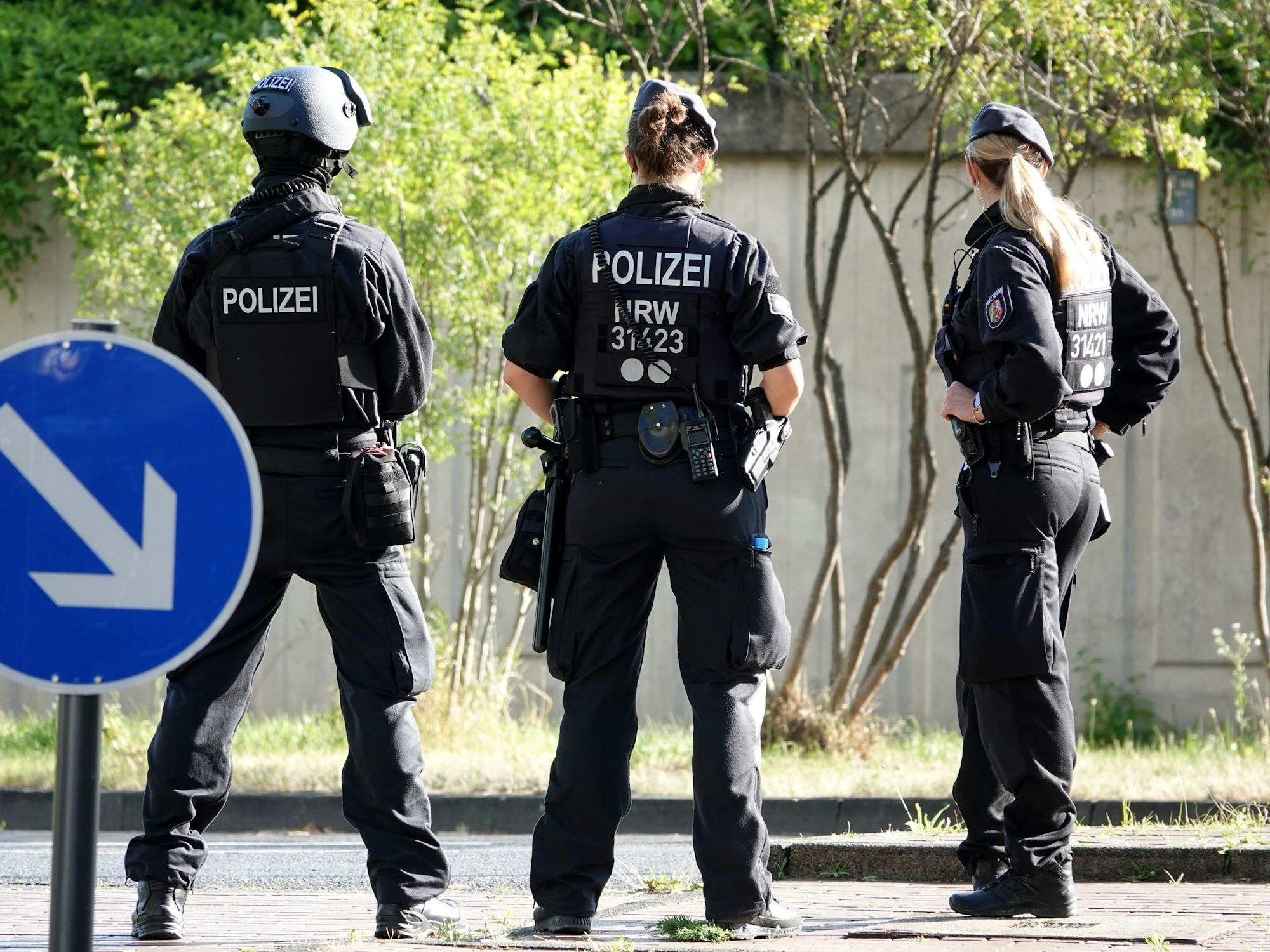 Drei Polizisten und Polizistinnen stehen mit dem Rücken zur Kamera auf einer Straße.