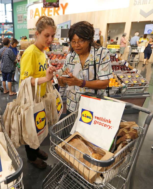 Auf diesem Foto vom 15. Juni 2017 ist zu sehen, wie eine Lidl-Mitarbeiterin zwei Kunden in Virginia Beach (USA) erklärt, wie die Lidl App funktioniert.