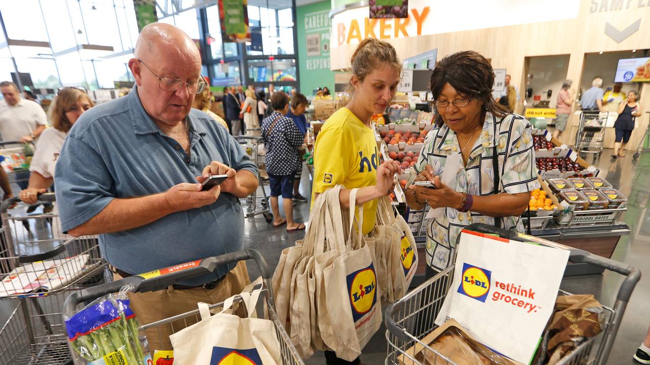 Auf diesem Foto vom 15. Juni 2017 ist zu sehen, wie eine Lidl-Mitarbeiterin zwei Kunden in Virginia Beach (USA) erklärt, wie die Lidl App funktioniert.
