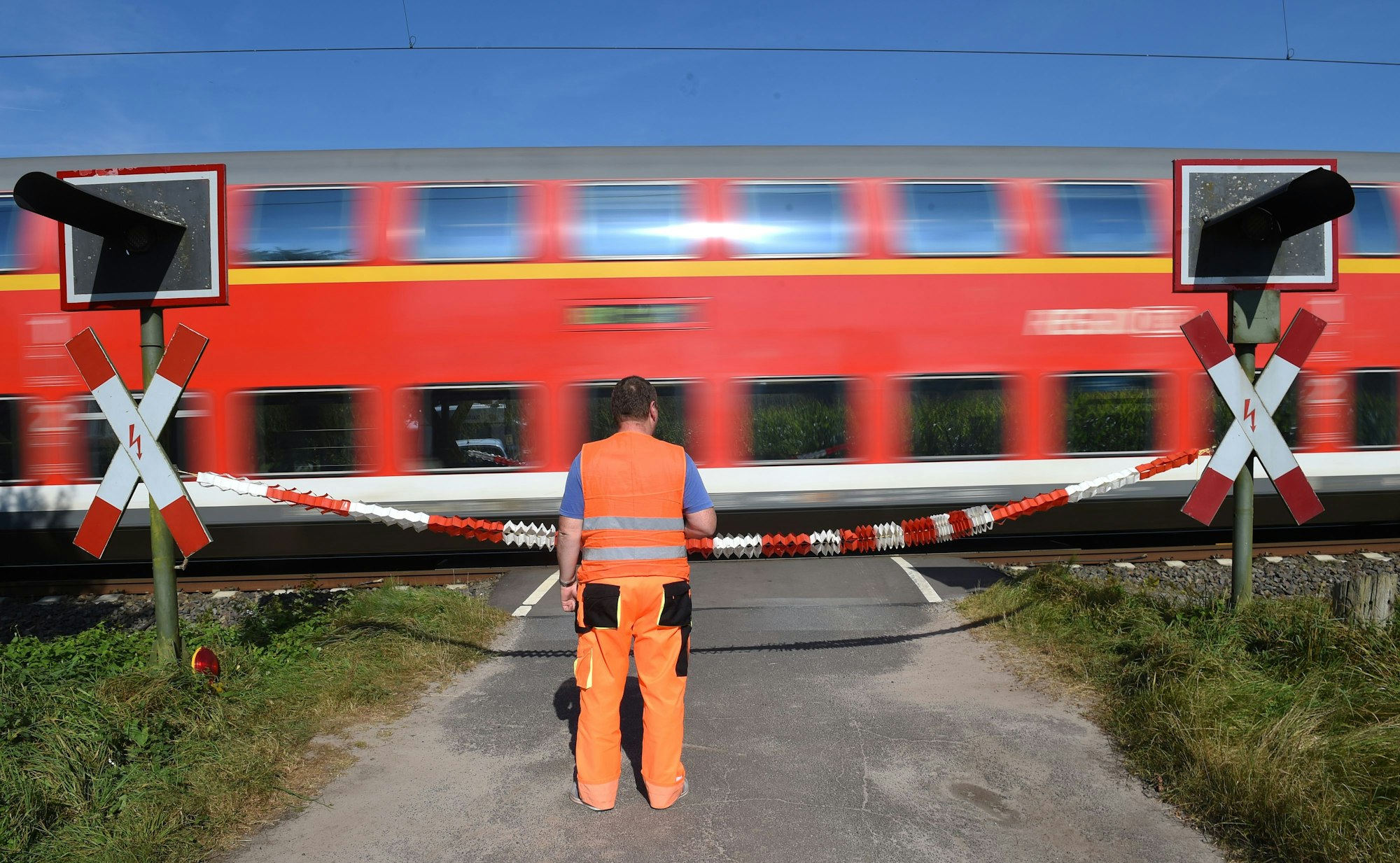 Das Symbolfoto, aufgenommen 2016, zeigt einen durchfahrenden Regionalzug an einem bewachten Bahnübergang.