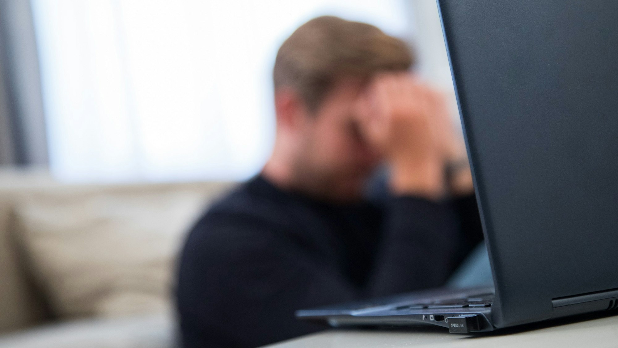 Das undatierte Symbolfoto zeigt einen aufgeklappten Laptop und einen Mann, der davorsitzt und den Kopf in die Hände stützt.
