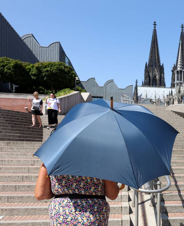 Zwei Erwachsene schützen sich mit Schirmen vor der Hitze.