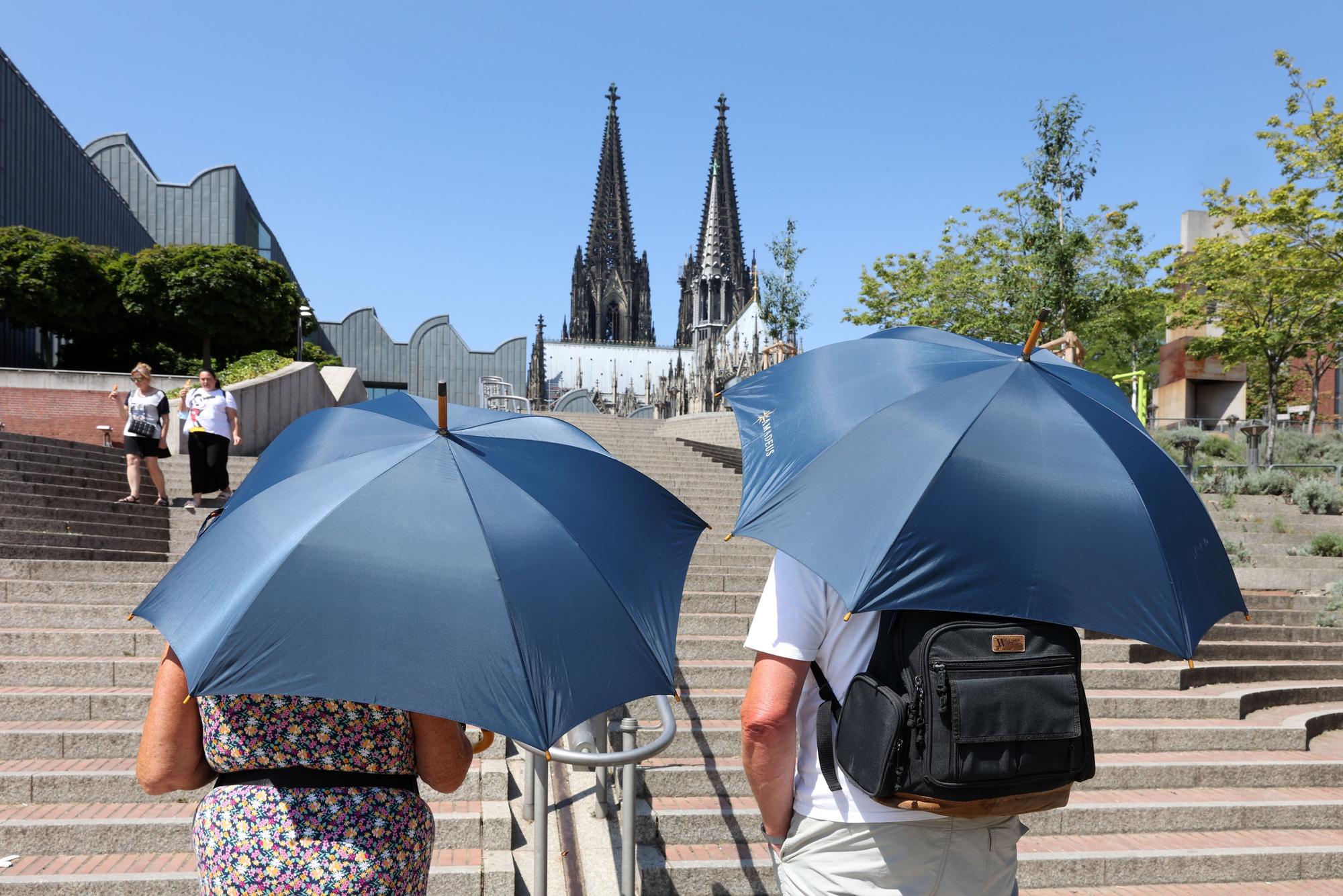 Zwei Erwachsene schützen sich mit Schirmen vor der Hitze.
