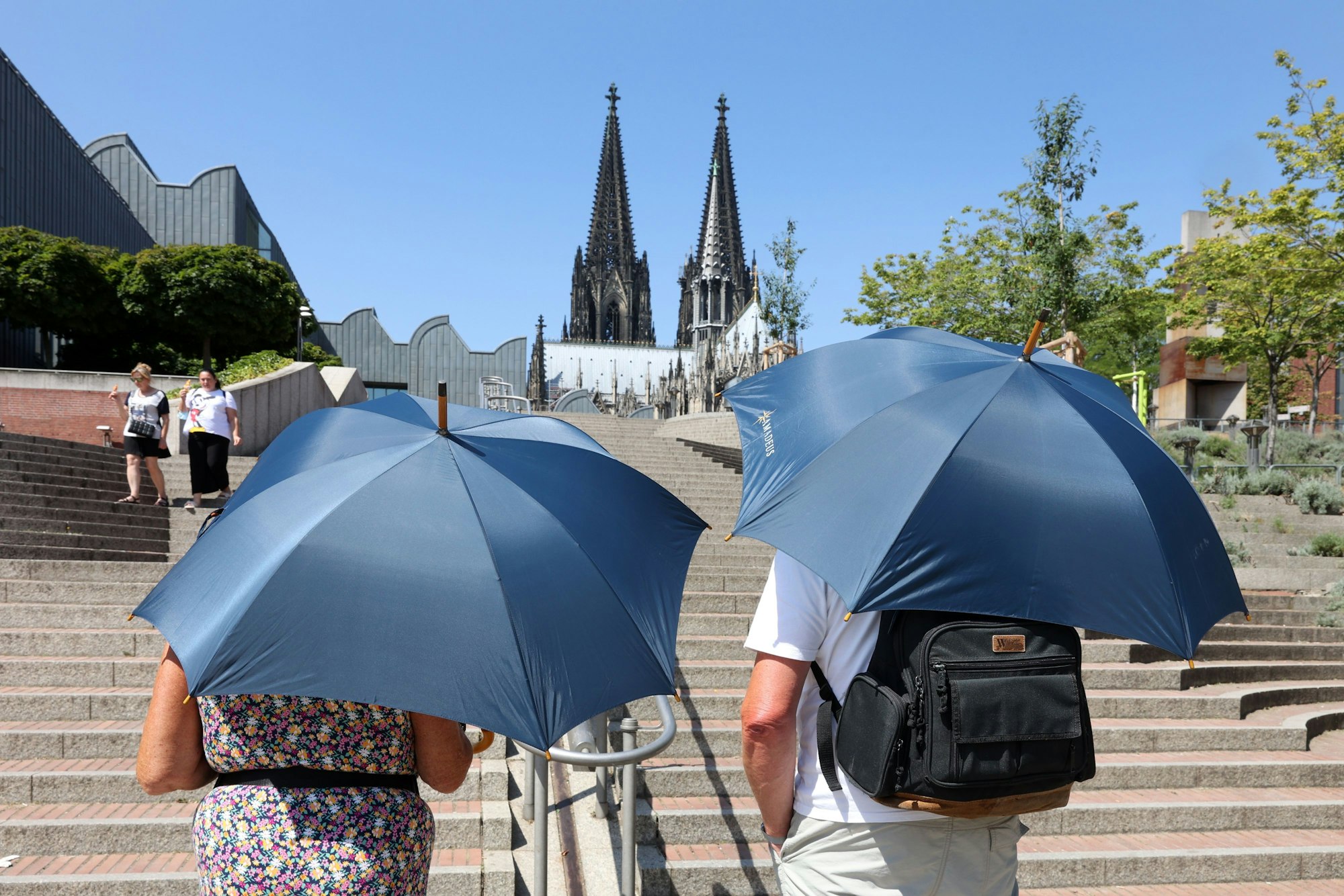 Zwei Erwachsene schützen sich mit Schirmen vor der Hitze.