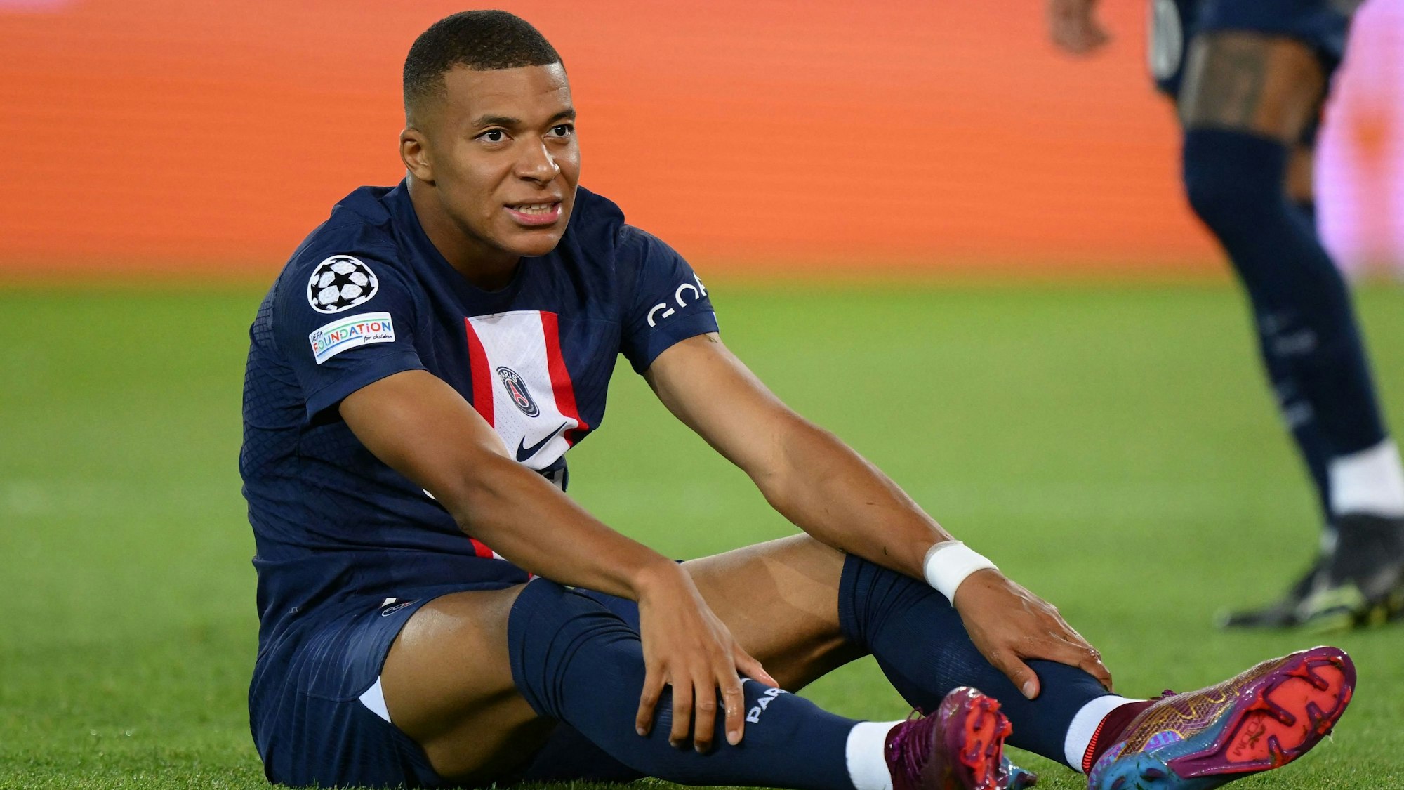 Kylian Mbappé sitzt bei einem Spiel von PSG auf dem Rasen.