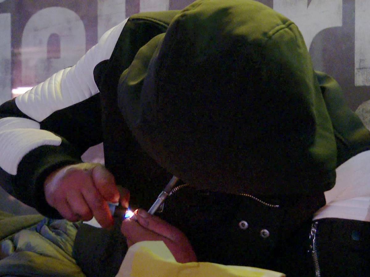 Heiko sitzt in einer schwarzen Kapuzenjacke vor einem Supermarkt und konsumiert Heroin.