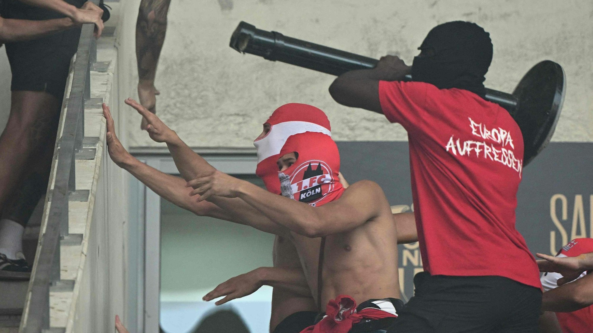 Maskierte Hooligans des 1. FC Köln nähern sich Anhängern vom OGC Nizza auf der Tribüne. Ein Kölner versucht, mit einem Absperrpfosten nach den Heimfans zu schlagen.
