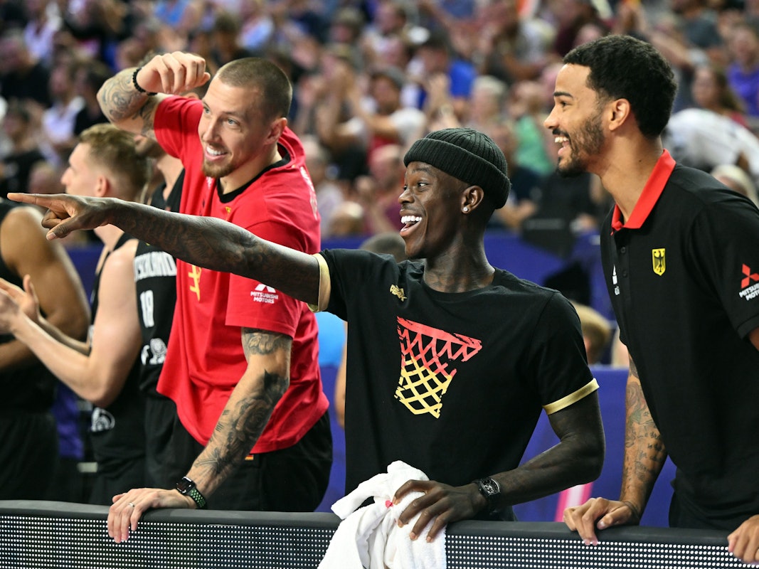 Deutschlands Daniel Theis (l.),Dennis Schröder und Nick Weiler-Babb verfolgen das Spiel auf der Bank.