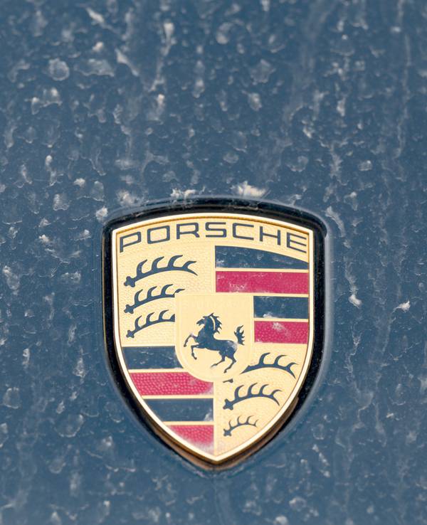 Ein Logo des Fahrzeugbauers Porsche ist an einer mit Wüstenstaub bedeckten Motohaube eines Sportwagens angebracht.