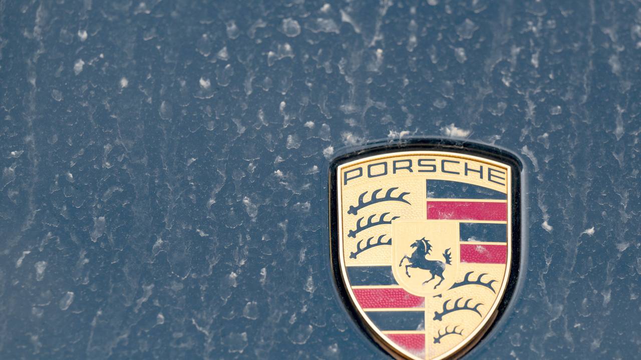 Ein Logo des Fahrzeugbauers Porsche ist an einer mit Wüstenstaub bedeckten Motohaube eines Sportwagens angebracht.