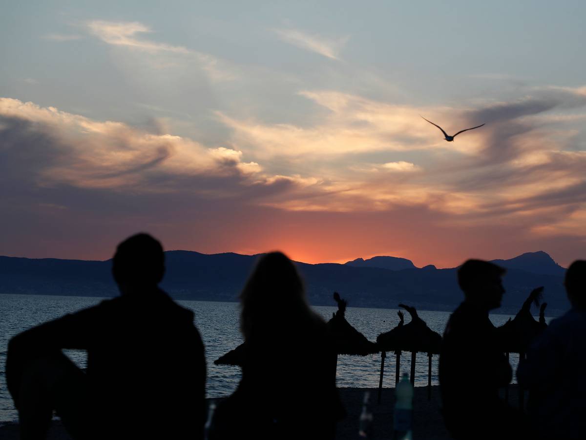 Junge Leute sitzen auf diesem undatierten Symbolfoto bei Sonennuntergang am Strand von El Arenal.