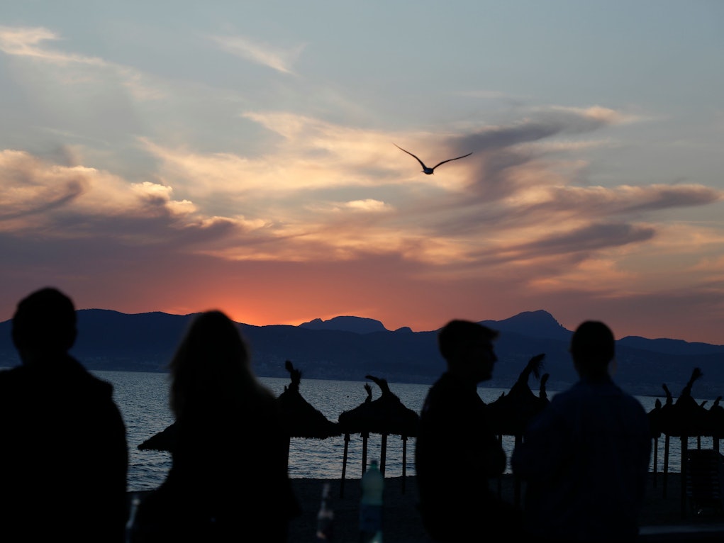 Junge Leute sitzen auf diesem undatierten Symbolfoto bei Sonennuntergang am Strand von El Arenal.