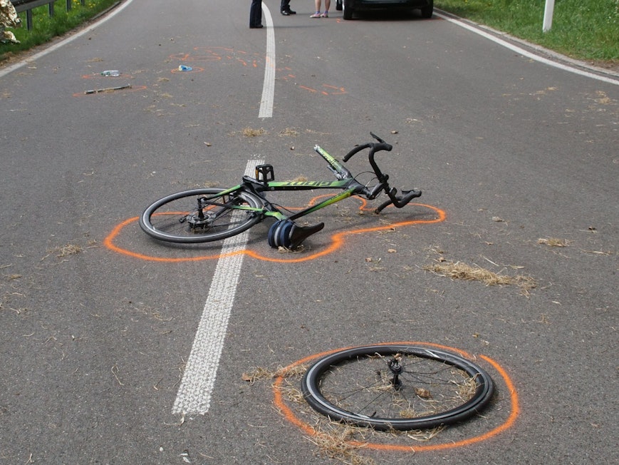 Der Vorderreifen eines Fahrrads liegt neben dem Fahrrad an einer Unfallstelle. Beides ist mit Markierungen der Polizei gekennzeichnet.