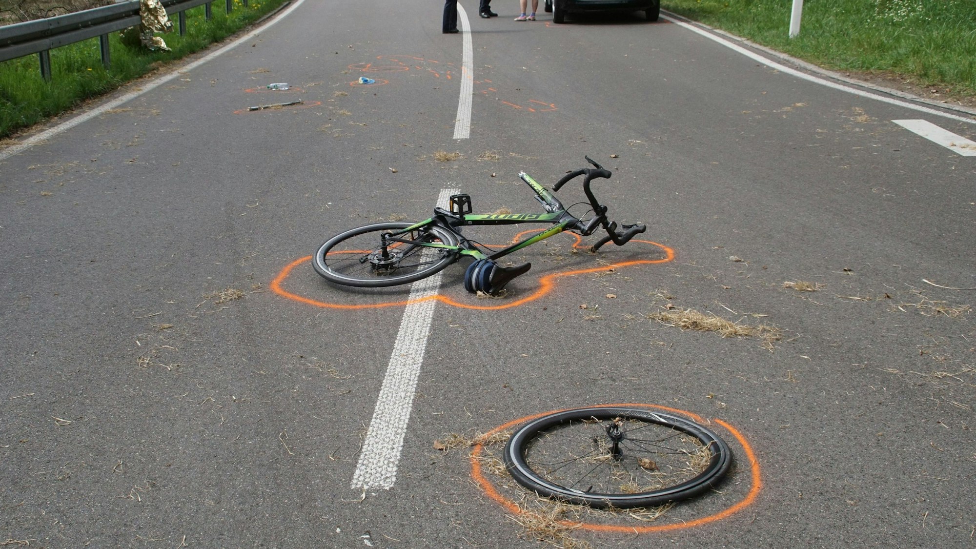 Der Vorderreifen eines Fahrrads liegt neben dem Fahrrad an einer Unfallstelle. Beides ist mit Markierungen der Polizei gekennzeichnet.