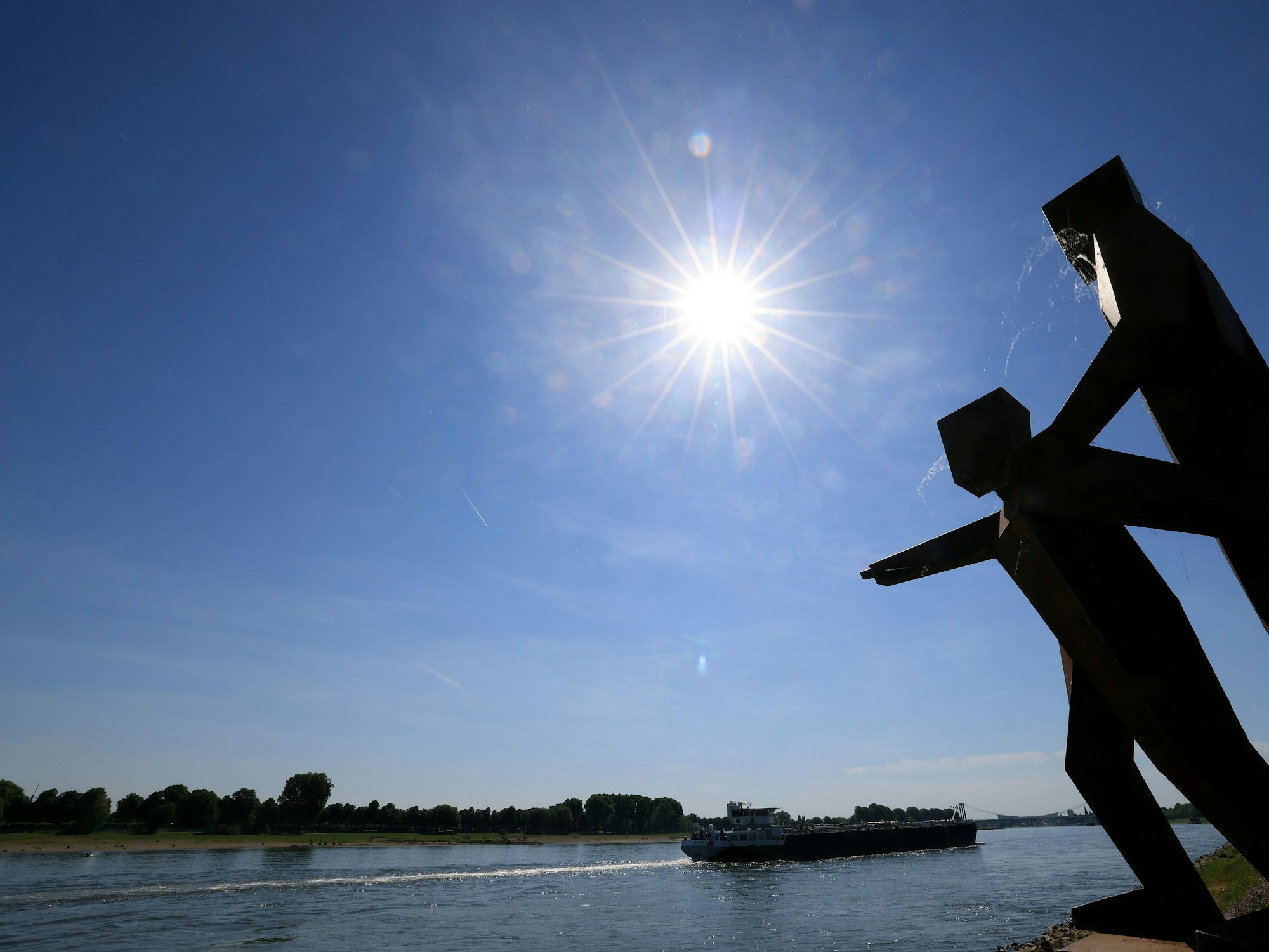 Die Sonne scheint am Rheinufer in Köln auf eine unbekannte Skulptur.+