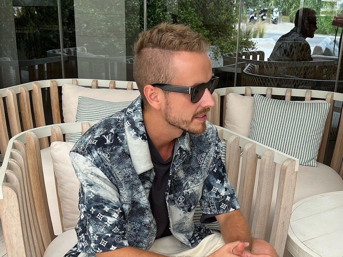 Influencer Julian Claßen, hier auf einem Instagram-Bild von Juni 2022, macht mit seiner neuen Freundin Tanja Makaric den nächsten Schritt. Julian sitzt in einem Korbstuhl, er trägt ein schwarz-weiß gemustertes Hemd und eine schwarze Sonnenbrille.