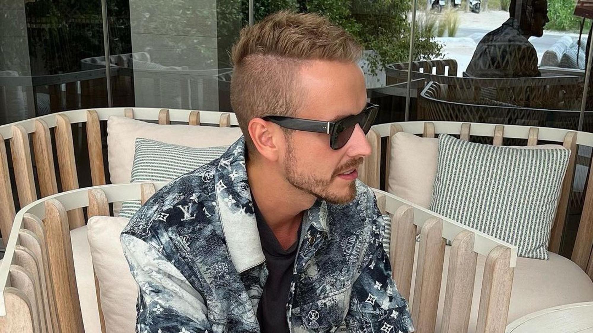 Influencer Julian Claßen, hier auf einem Instagram-Bild von Juni 2022, macht mit seiner neuen Freundin Tanja Makaric den nächsten Schritt. Julian sitzt in einem Korbstuhl, er trägt ein schwarz-weiß gemustertes Hemd und eine schwarze Sonnenbrille.