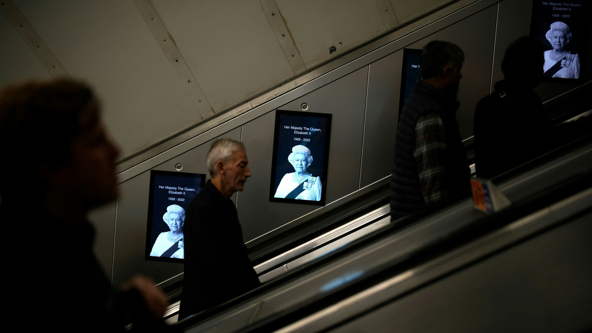 Pendler gehen in der Londoner U-Bahn an Fotos von Königin Elizabeth II. vorbei.