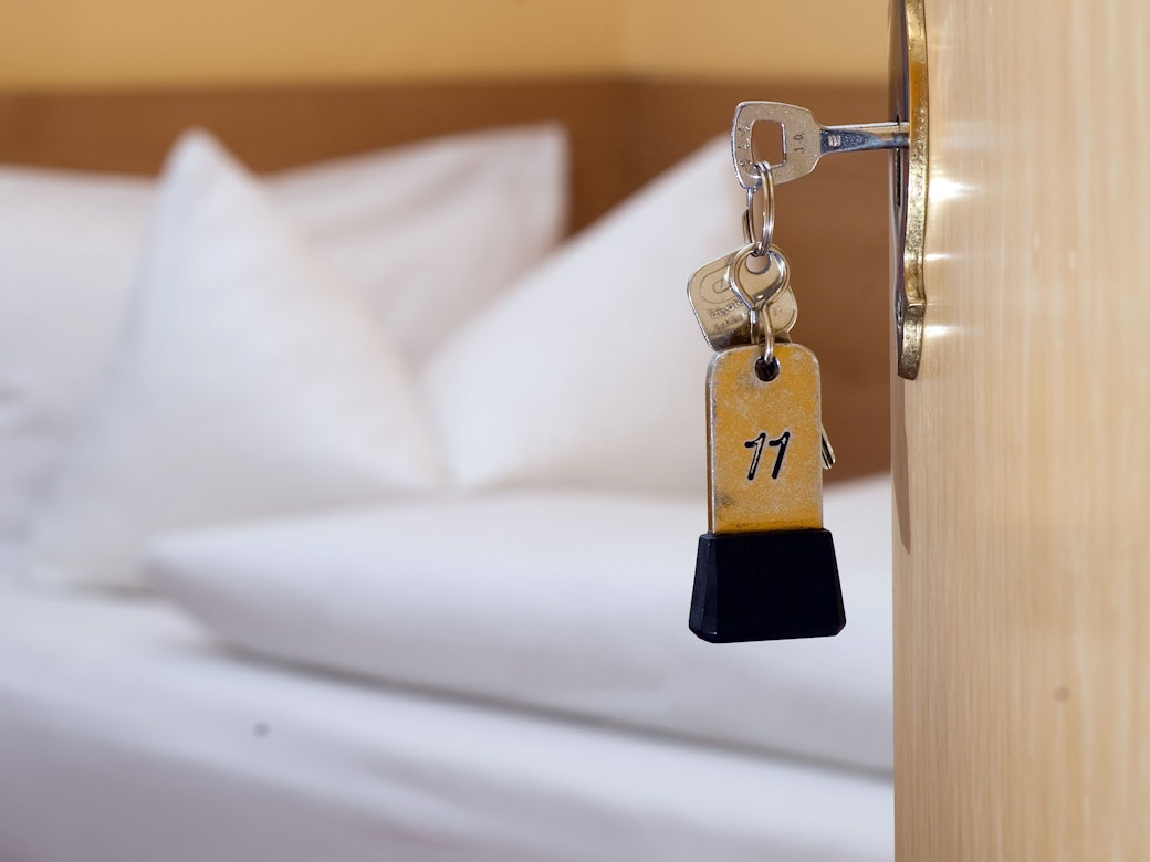 Ein Zimmerschlüssel hängt in einem Gästehaus vor einem Bett im Türschloss.