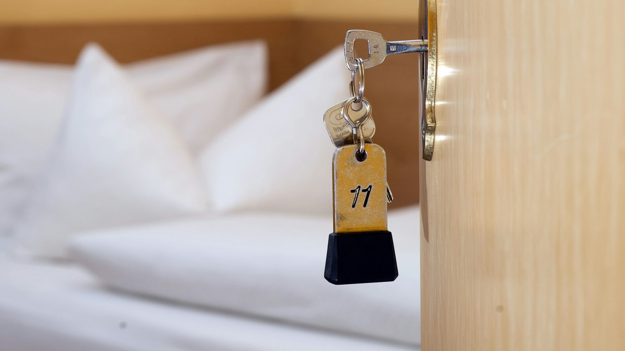 Ein Zimmerschlüssel hängt in einem Gästehaus vor einem Bett im Türschloss.