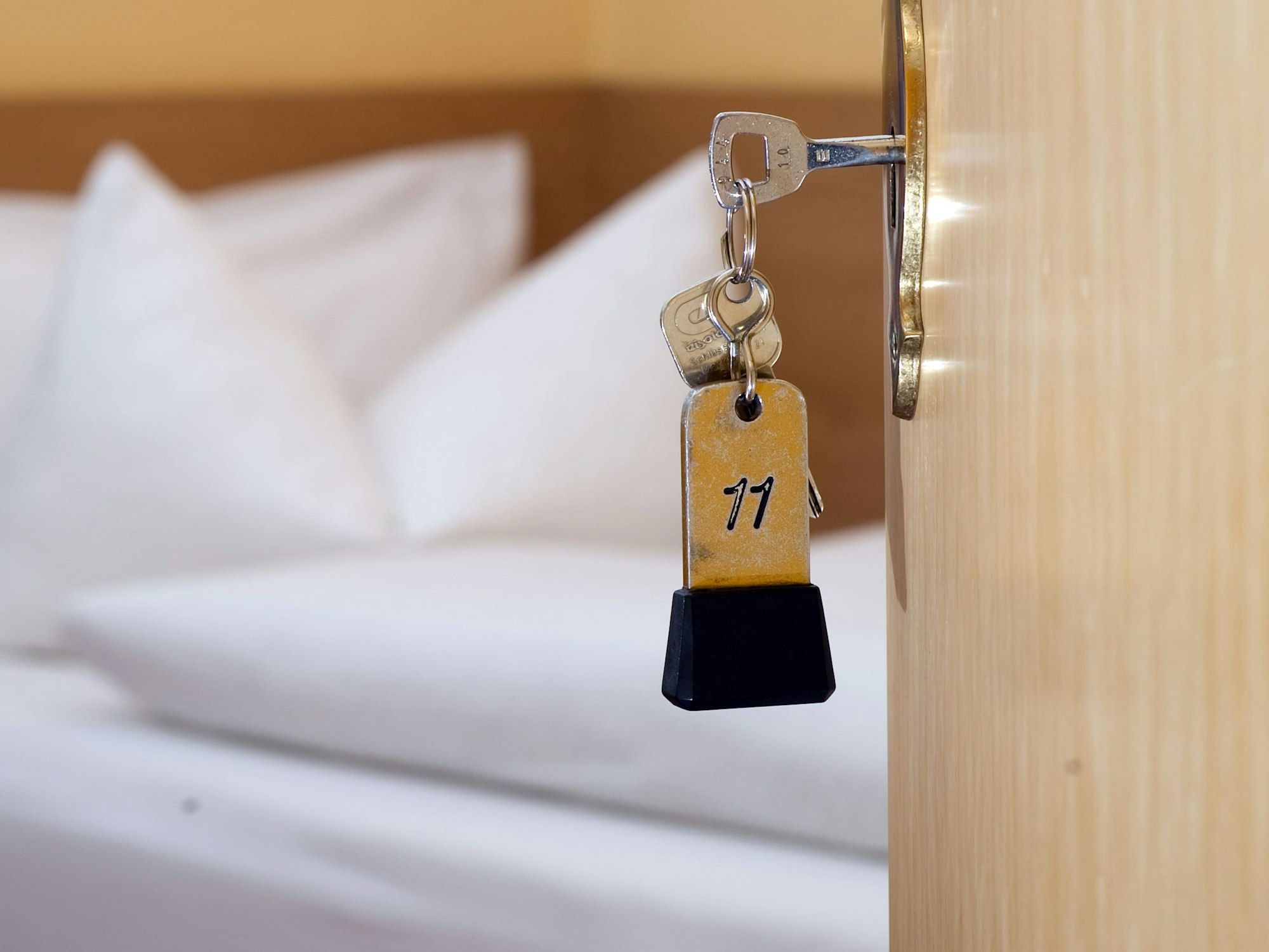 Ein Zimmerschlüssel hängt in einem Gästehaus vor einem Bett im Türschloss.