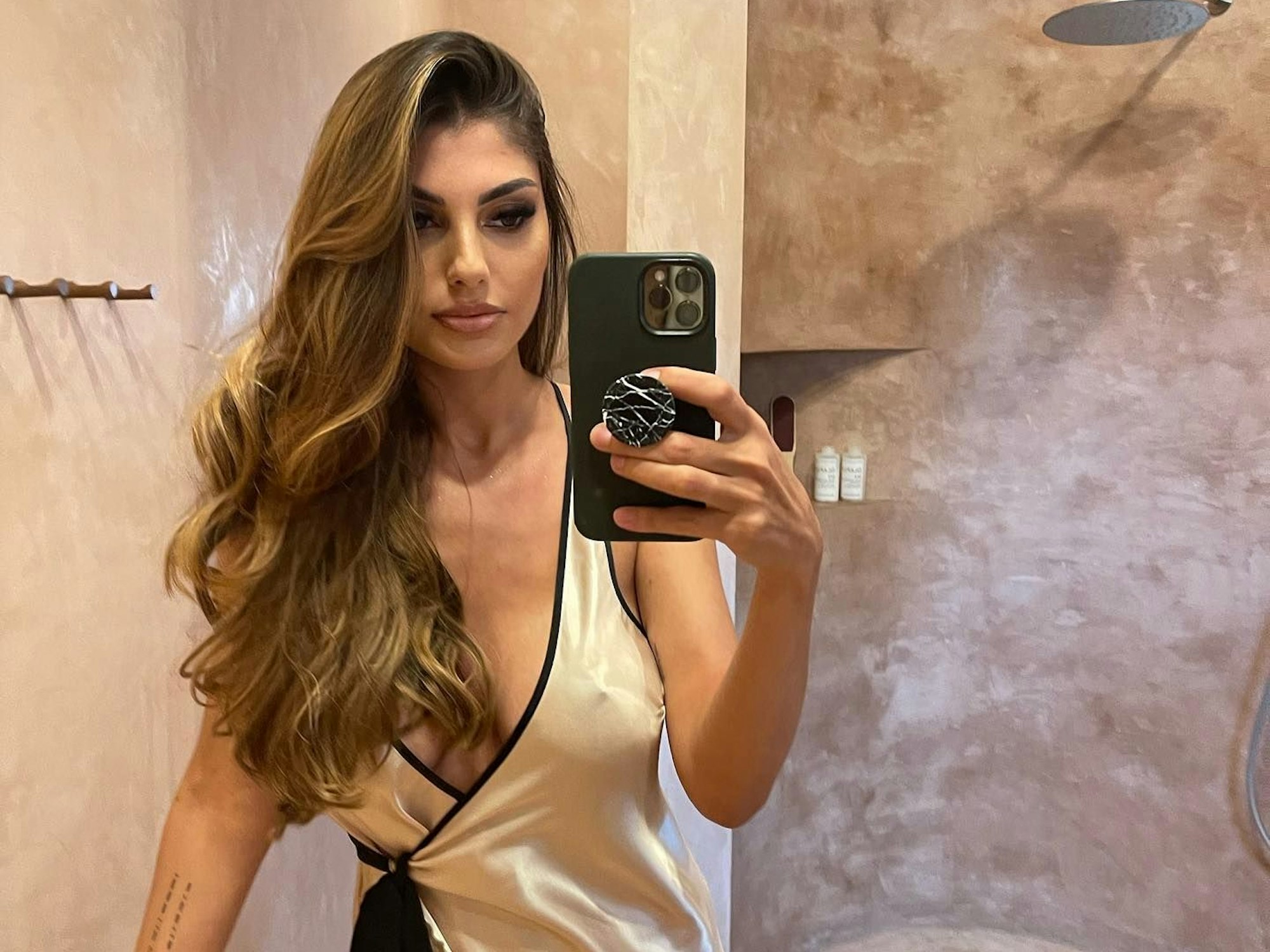 Yeliz Koc posiert in einem tief ausgeschnittenen Kleid vor einem Spiegel. Ihre Haare trägt sie offen zur Seite.