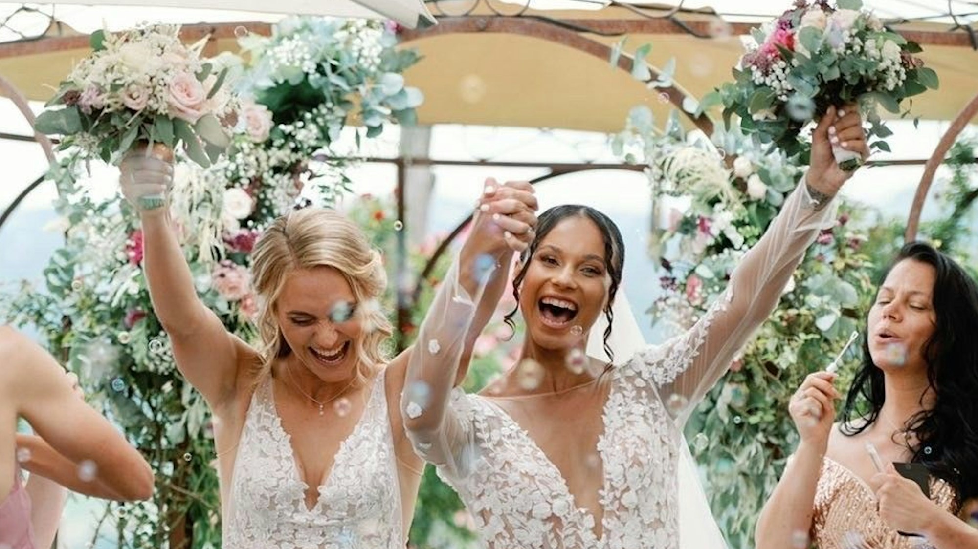 Sarah (l.) und Genessee Puntigam halten ihre Blumensträuße bei ihrer Hochzeit in die Höhe