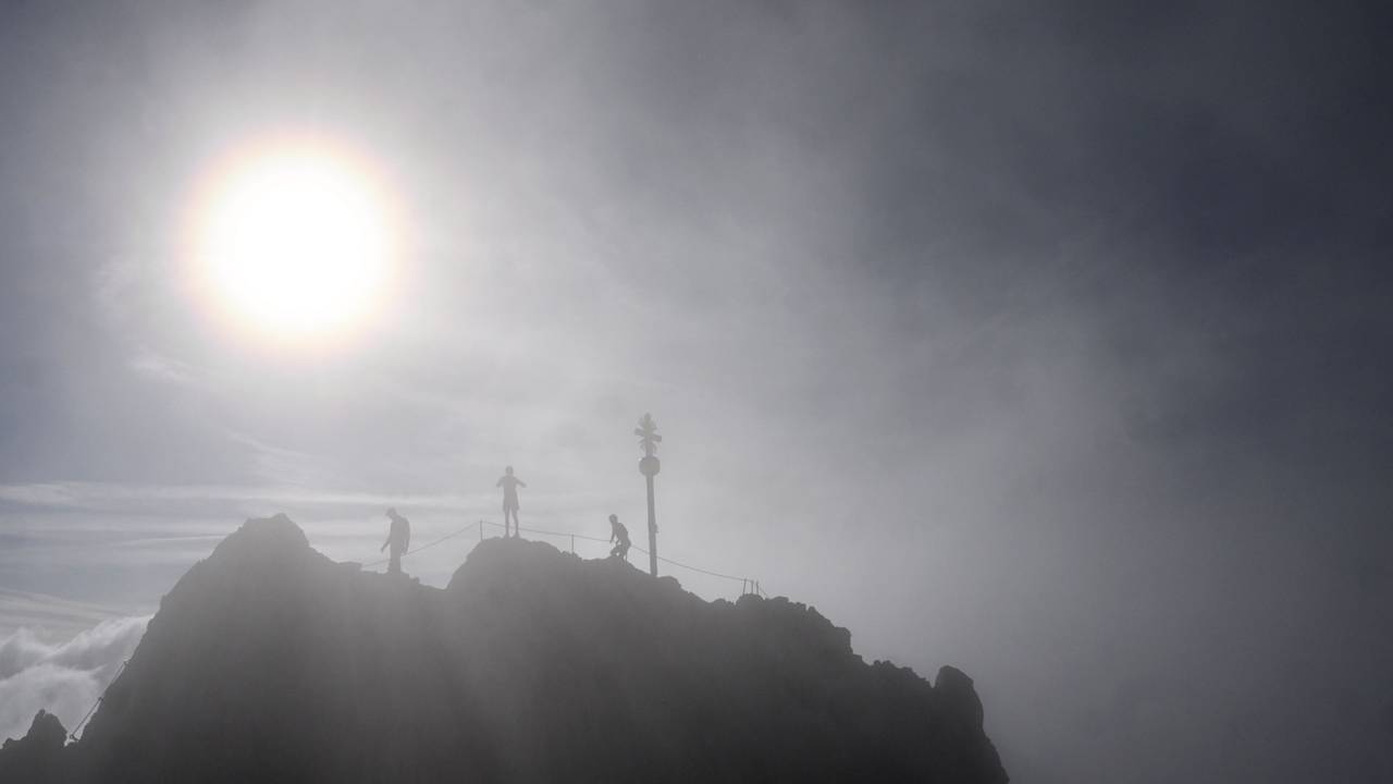 Drei Bergsteiger stehen neben dem Gipfelkreuz der Zugspitze.