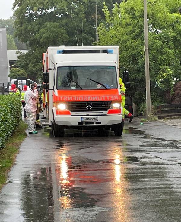 Einsatzkräfte in Schutzanzügen wuseln um einen Rettungswagen.